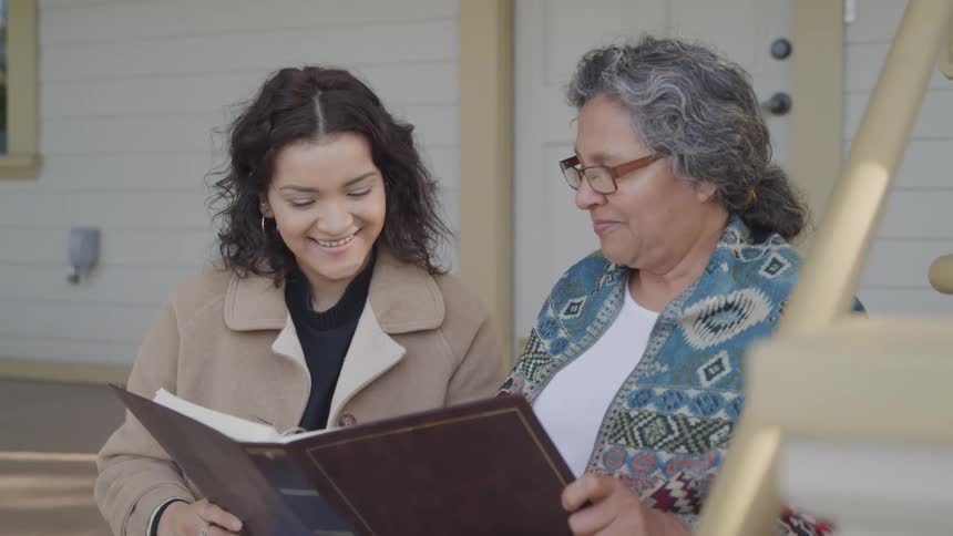 A grandmother and her granddaughter read a book on the porch