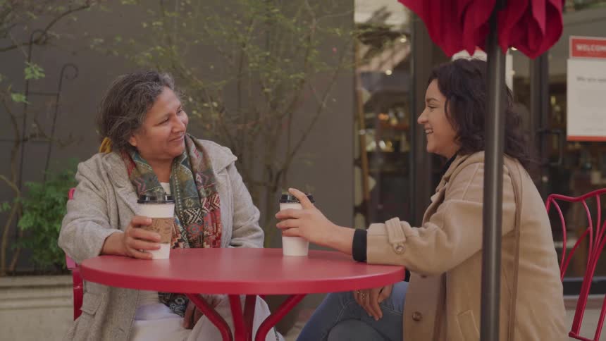 Two people sit at an outdoor caf holding coffee cups and engaged in conversation