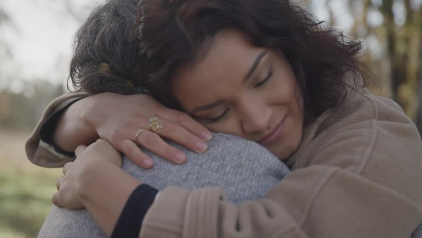 A young woman warmly hugs an older person outdoors