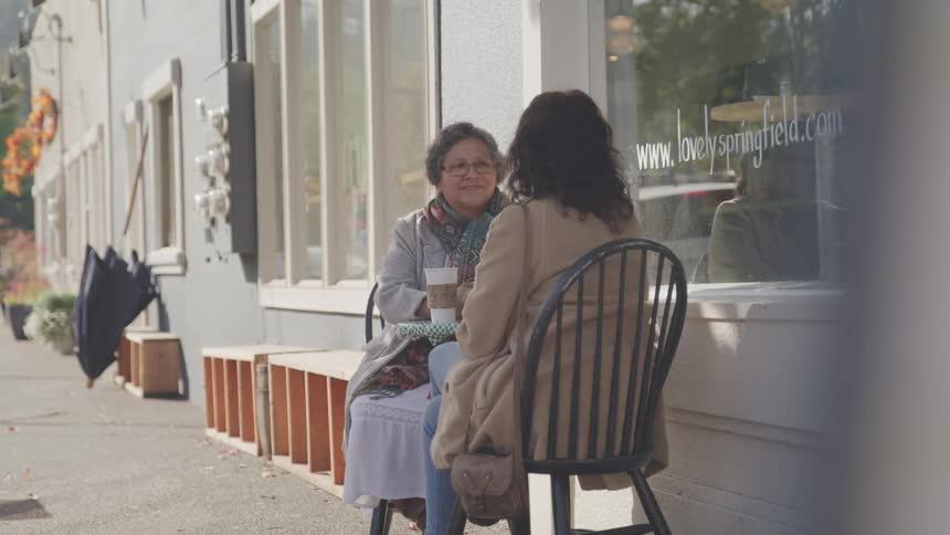 Two women sit outside a cafe with their drinks on a sunny autumn day