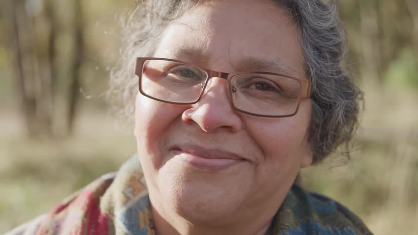 An older woman smiles gently at the camera in a closeup outdoor portrait