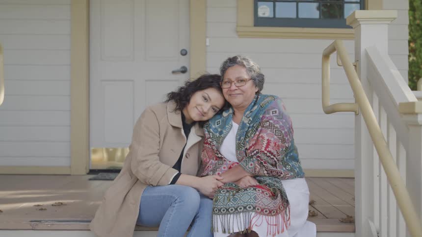 Young woman sitting next to an elderly lady on the outside stairs of a house