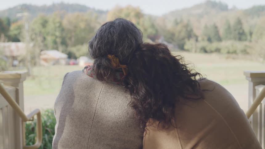 Mother and daughter sit close on outdoor steps one resting her head on the others shoulder