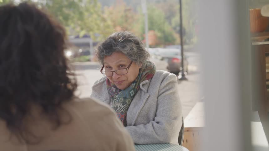 Two women are sitting and talking on the sidewalk
