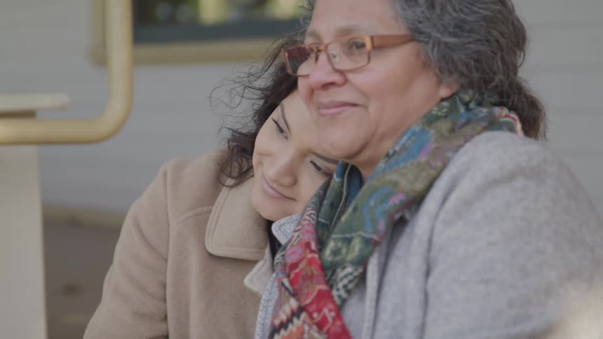 Elderly lady and a young woman hugging while sitting outside