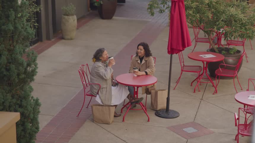 Two women are enjoying drinks and conversation at an outdoor caf
