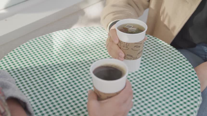 Two female hands holding two cups of hot coffee on a table at daytime