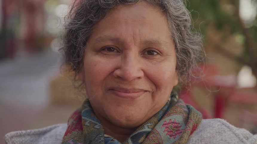 Elderly woman wearing a colorful scarf smiles while standing outdoors