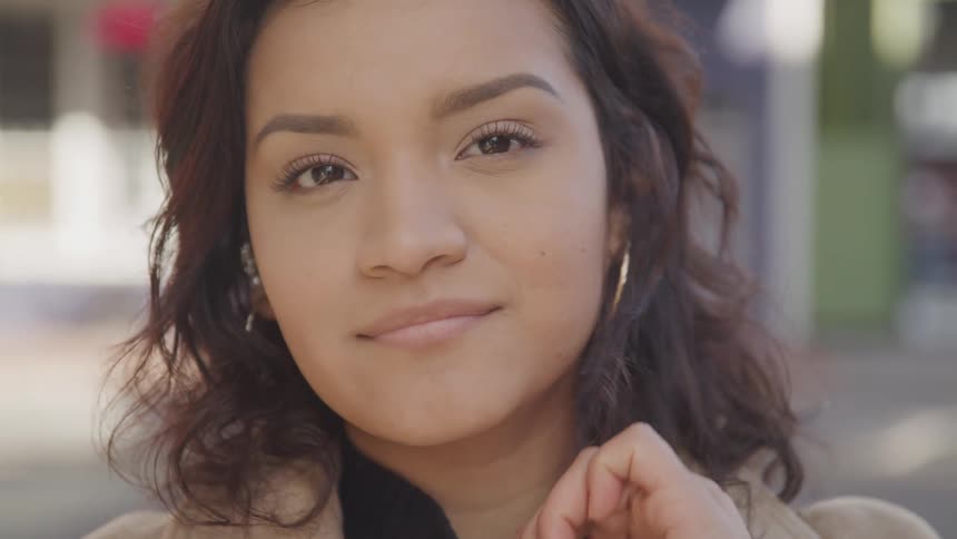 The face of a young woman who is looking mostly straight ahead and tucking her hair behind her ear