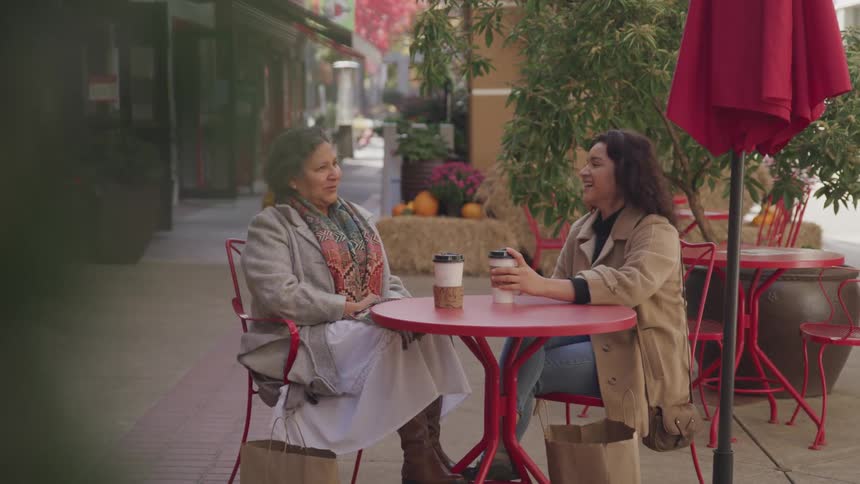 Two women sitting in an outdoor patio laughing and tallking at a coffee shop