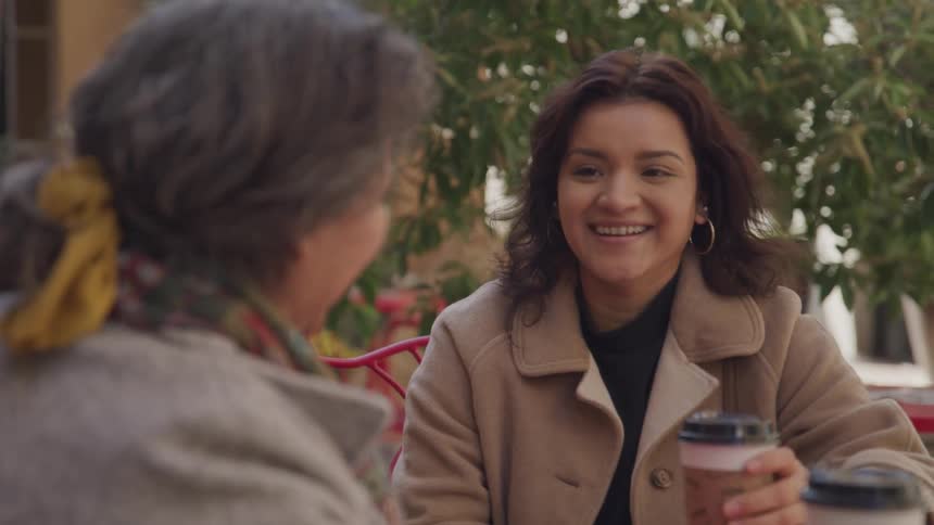 Two women share a joyful coffee conversation at an outdoor caf