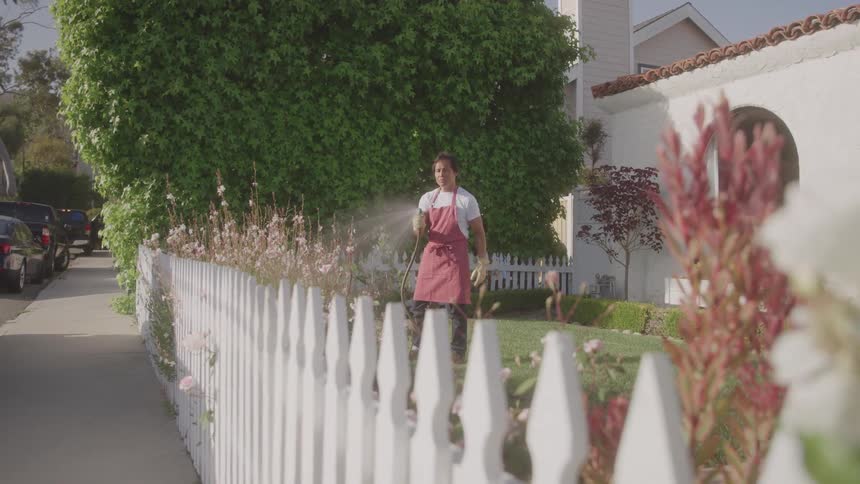 A gardener watering garden plants with a hose