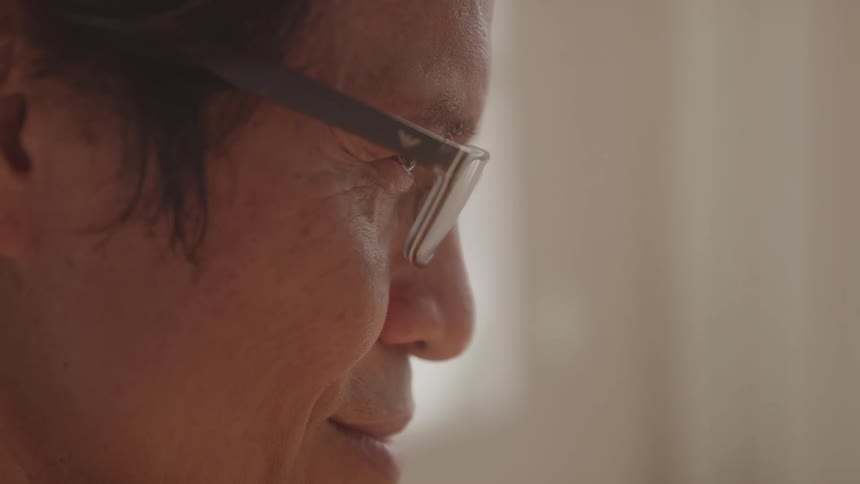 A man with dark hair and glasses looks towards the right side of the frame