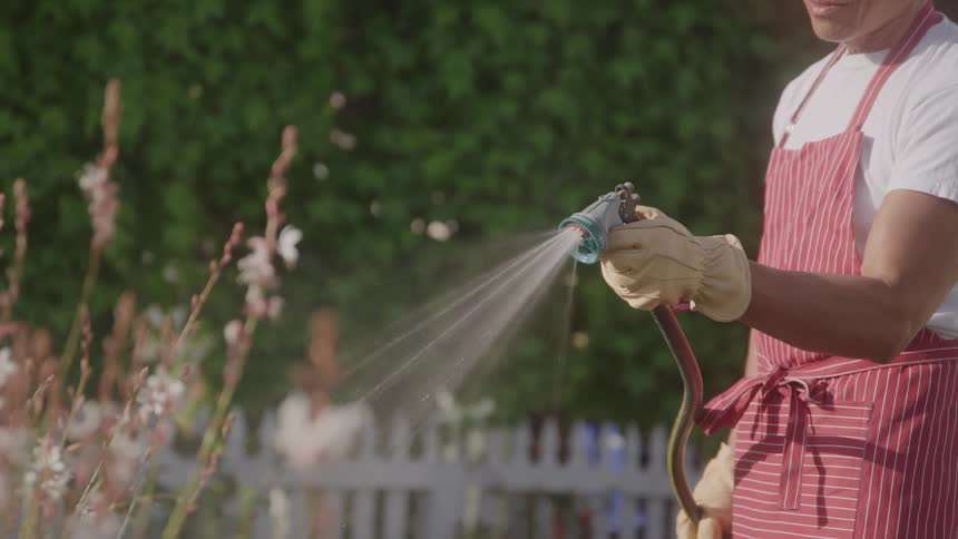 A man sprinkles water on outdoor plants during the day