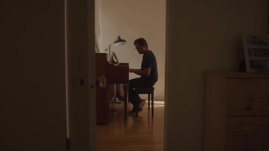 A man plays the piano alone in a warmly lit room