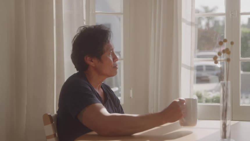 A middleaged man sits at a coffee table drinking coffee from a mug around midday