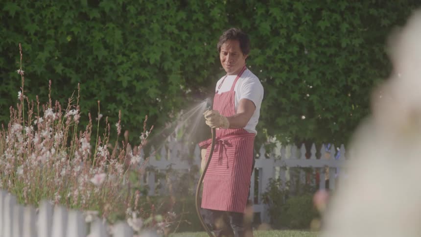 A man watering flowers in a wellkept garden on a sunny day