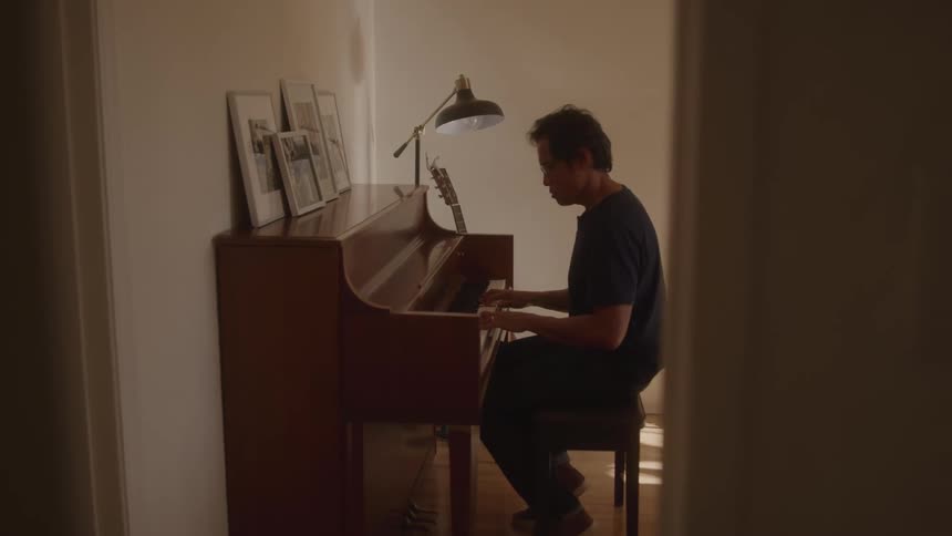 A man is quietly playing the piano alone in a warmly lit room
