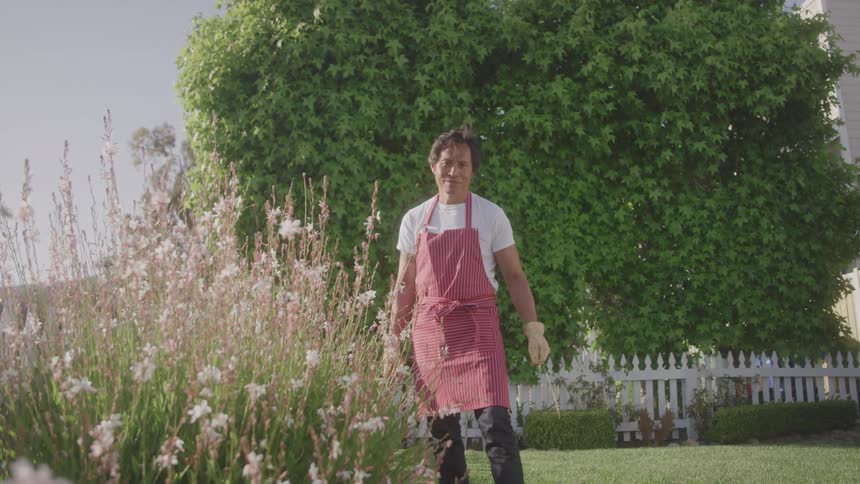 A man in a red apron standing ingarden with blooming flowers on a sunny day