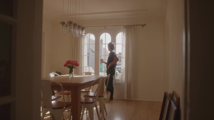 A man stands by the kitchen door holding a mug and gazing out through the window