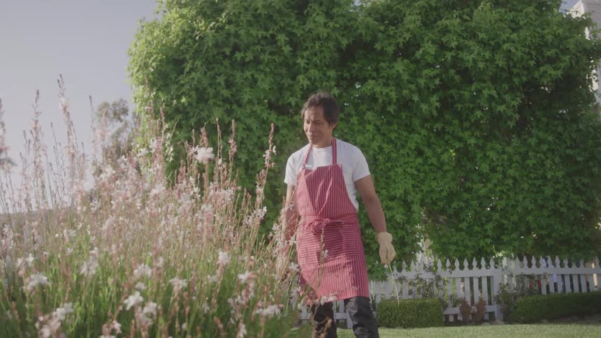 Man in a red apron proudly standing next to his garden in his backyard