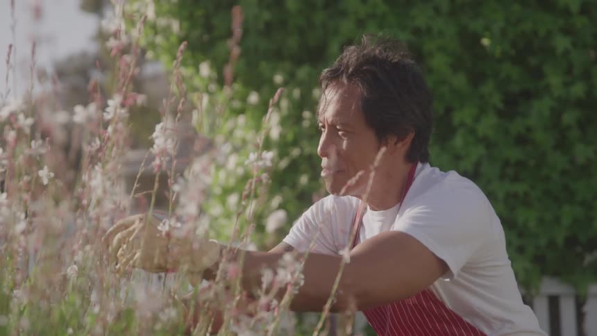 Asian man in a white tshirt and red apron tending to his garden