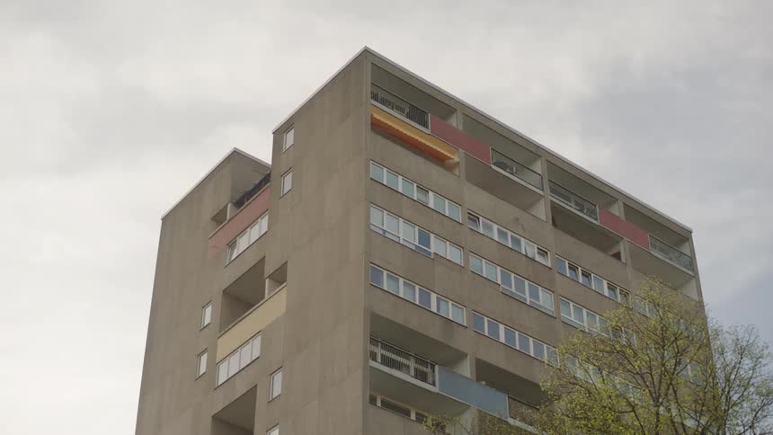 A tall apartment building is viewed from below against a cloudy sky