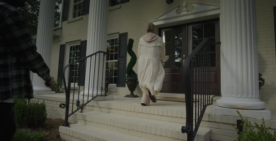 A family of three walks up the steps of a white columned house at dusk