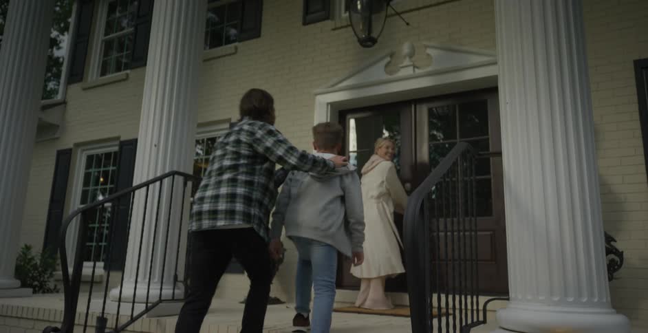 A family walks up the steps to enter a large house seemingly exploring their new home