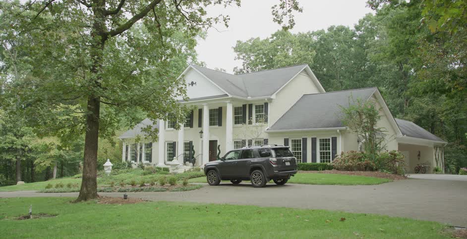 A parked car in front of a suburban house surrounded by trees at dawn