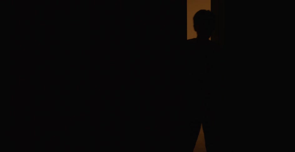 A child steps through a dimly lit doorway into a completely dark room
