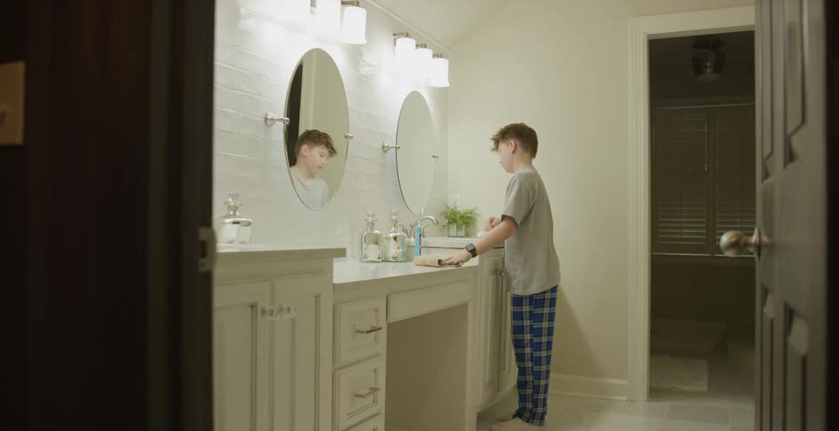 Boy wipes his hands with a towel while standing at a bathroom sink