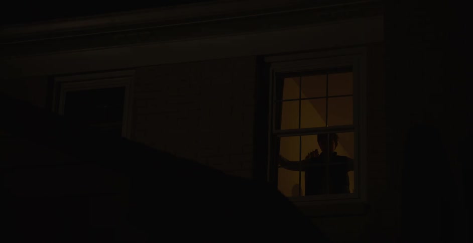 Silhouette of a boy opening the curtain of a window in a house at night