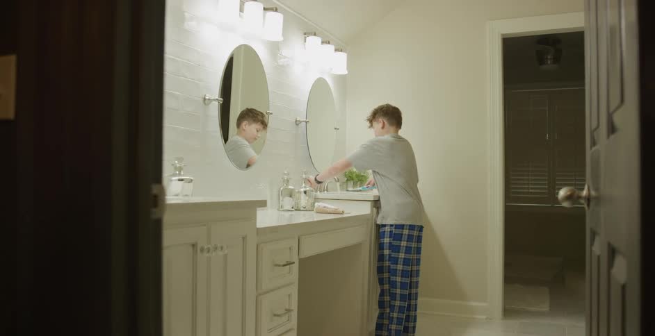 Male teenager walks to the sink in the bathroom with his toothbrush to brush his teeth