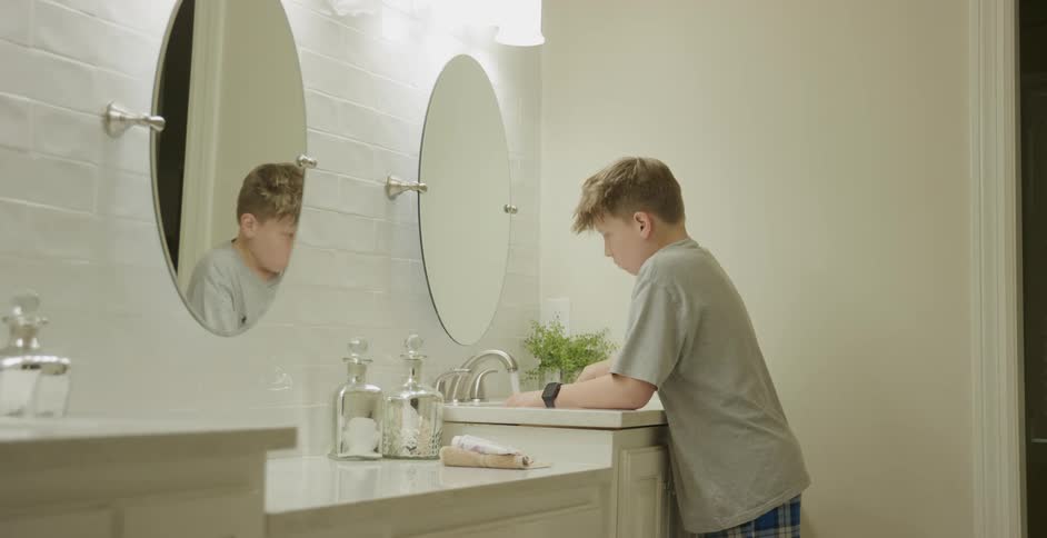 A young boy is brushing his teeth while looking at himself in the bathroom mirror
