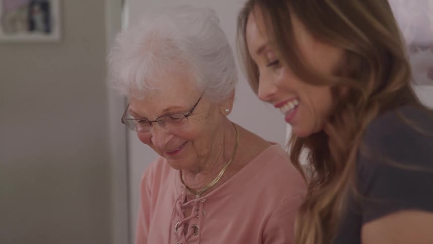 An elderly woman and a younger woman share a warm joyful moment together indoors