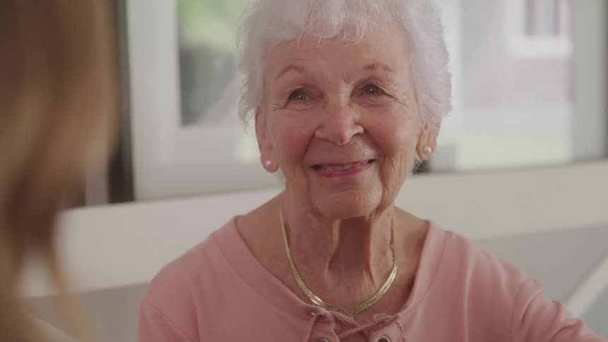Elderly woman sitting indoors smiles at a younger woman