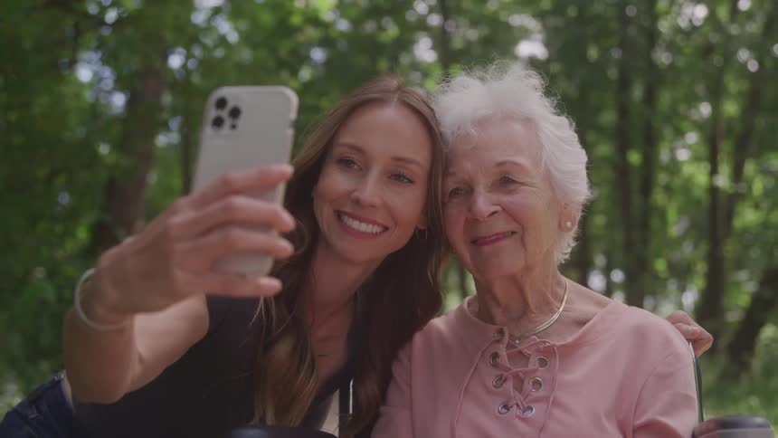 Young woman takes a selfie with an elderly woman outdoors during daytime