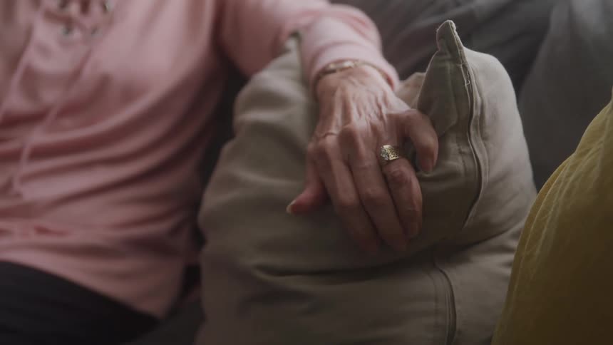 Elderly woman sitting on a couch with her hand resting on a gray pillow