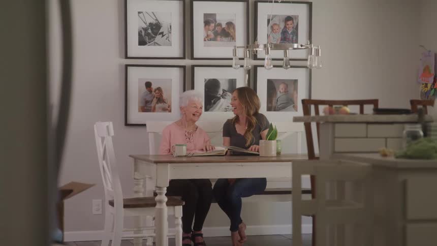 A grandmother and granddaughter laugh while looking in a book
