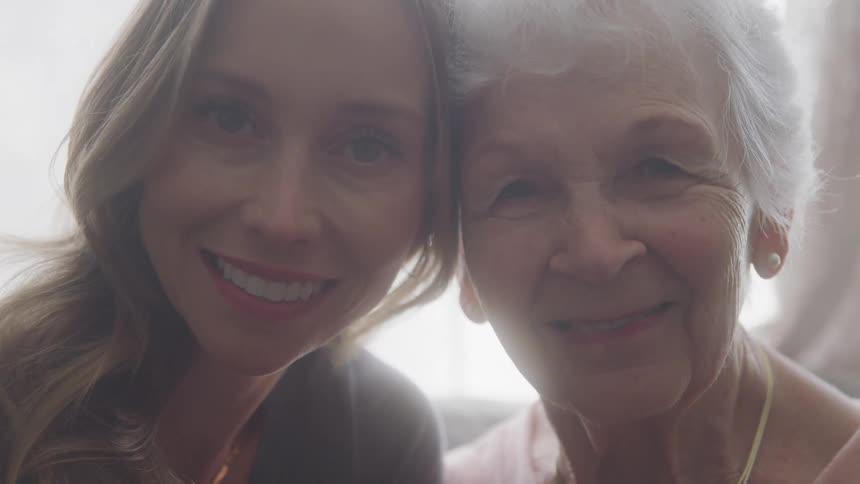 Two women lean heads together smiling