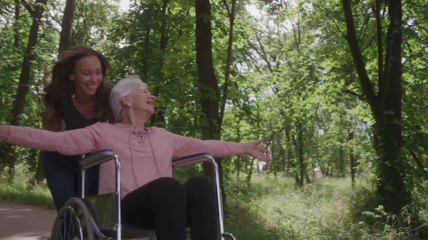 Woman running with elderly lady in wheelchair with open arms happy