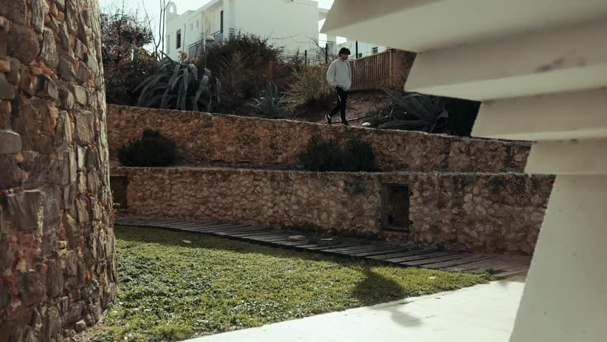 A person walks down a street surrounded by grasses around midday