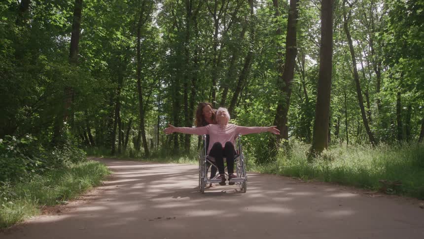 Woman quickly pushes her mother in a wheelchair along a path through the woods