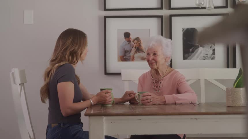 A young woman and an elderly lady enjoy a warm conversation over coffee at a kitchen table