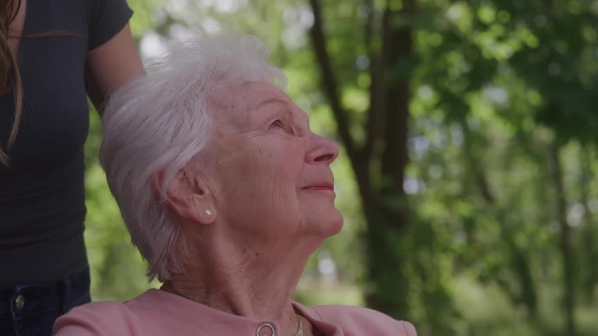 An elderly woman smiles gently while looking up surrounded by nature
