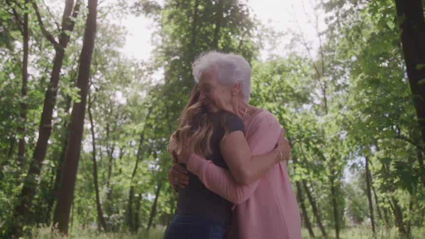 Elderly woman hugging her grandaughter in a forest area surrounded by trees