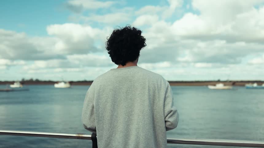 Curly haired man enjoying seaside view with boats