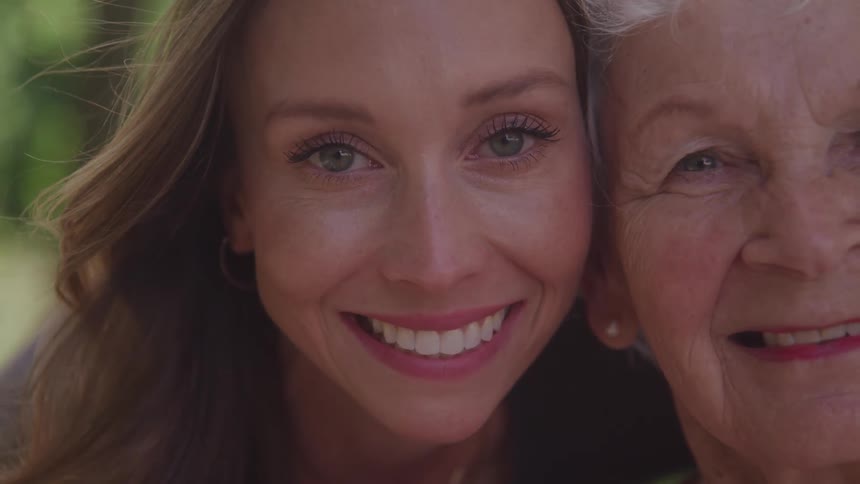 A young woman and an elderly woman close together smiling and looking forward