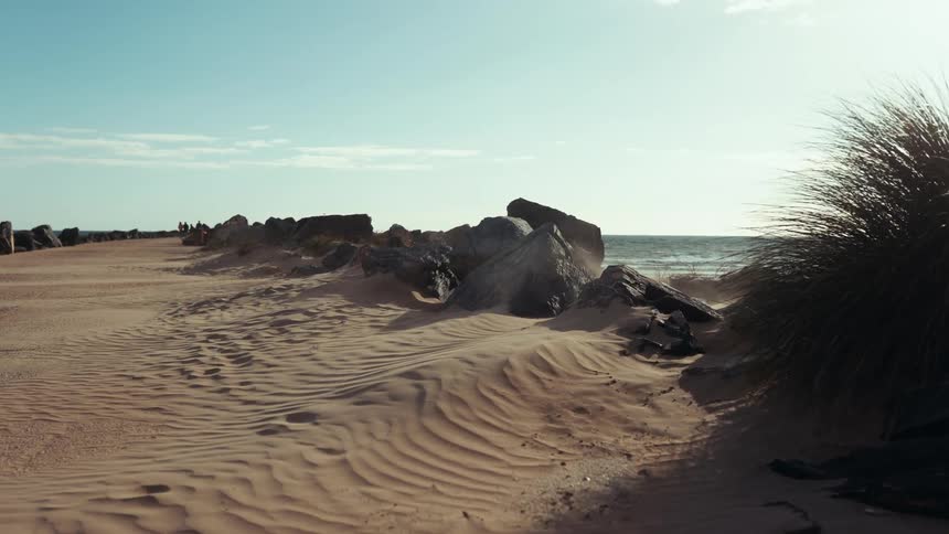 A scenic coastal landscape featuring sand dunes large rocks and beach grass under a